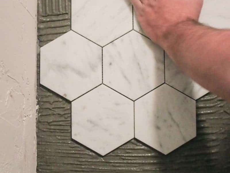 Installer pressing hexagon marble tile into place on a bathroom wall, Miami