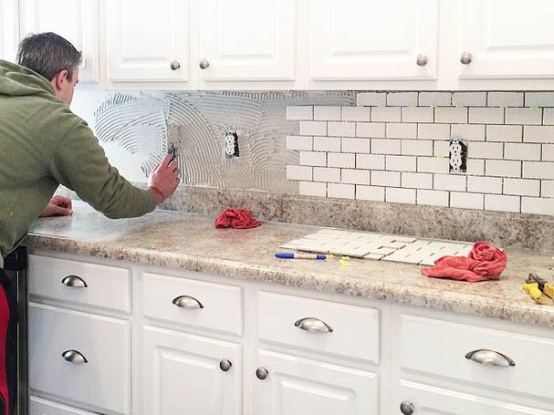 Installer setting a white subway tile backsplash above a kitchen countertop, Miami